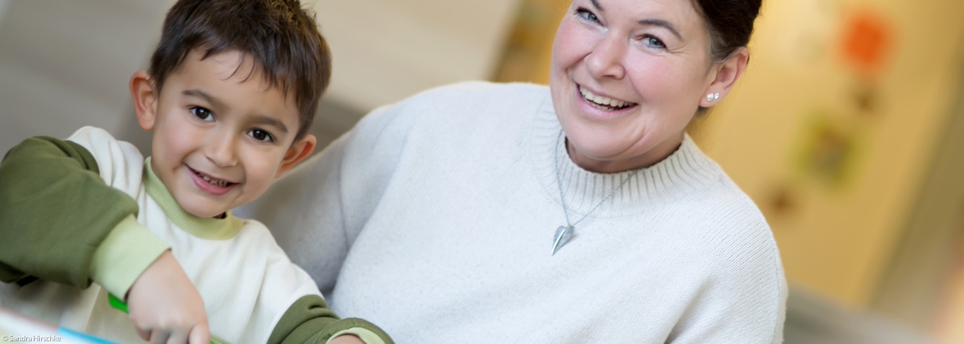 Eine Erzieherin hilft einem Kind beim Gemüseschneiden